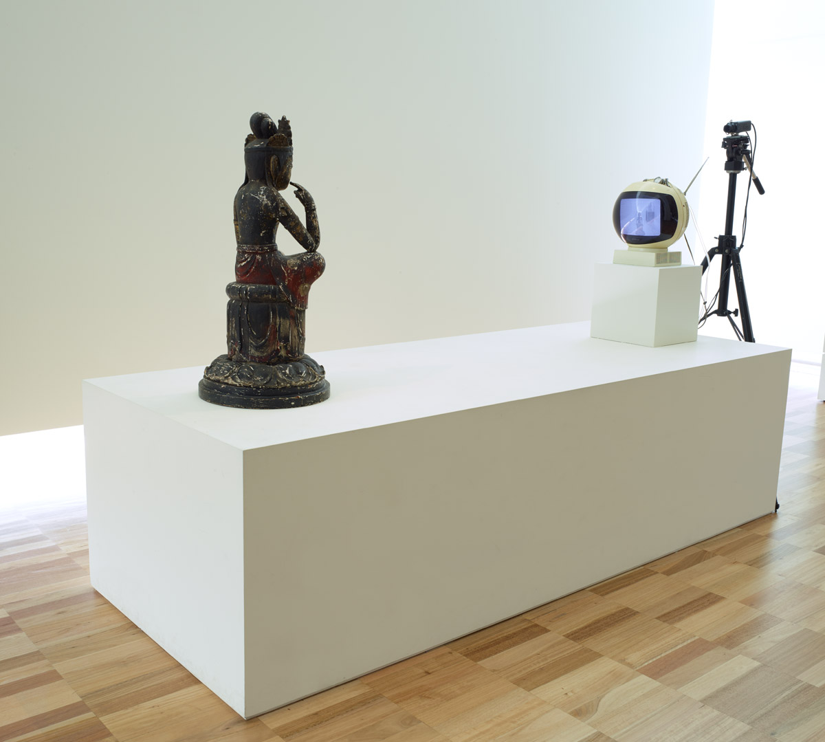 Nam June Paik, TV Buddha, 1976, television monitor, video camera, painted wooden Buddha, tripod, plinth, installation dimensions variable.  Art Gallery of New South Wales Gift of the John Kaldor Family Collection 2011. Donated through the Australian Government's Cultural Gifts Program.  © Nam June Paik Estate 